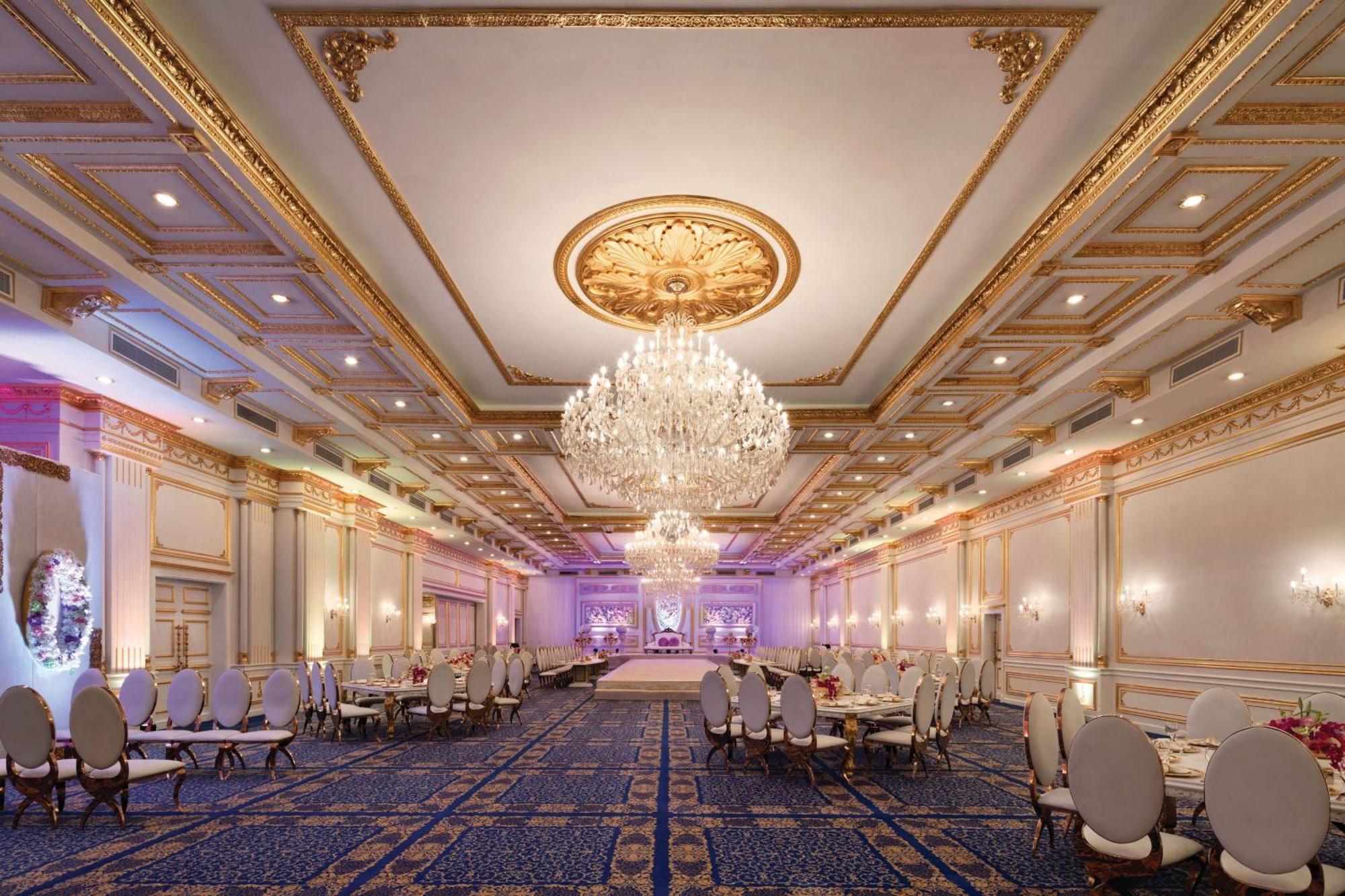 Grand Regency Doha, Trademark Collection By Wyndham Bagian luar foto The photo shows an elegant banquet hall with luxurious decor. The room features high ceilings adorned with intricate gold details and a large chandelier that hangs in the center, providing soft illumination. There are several round tables with plush 