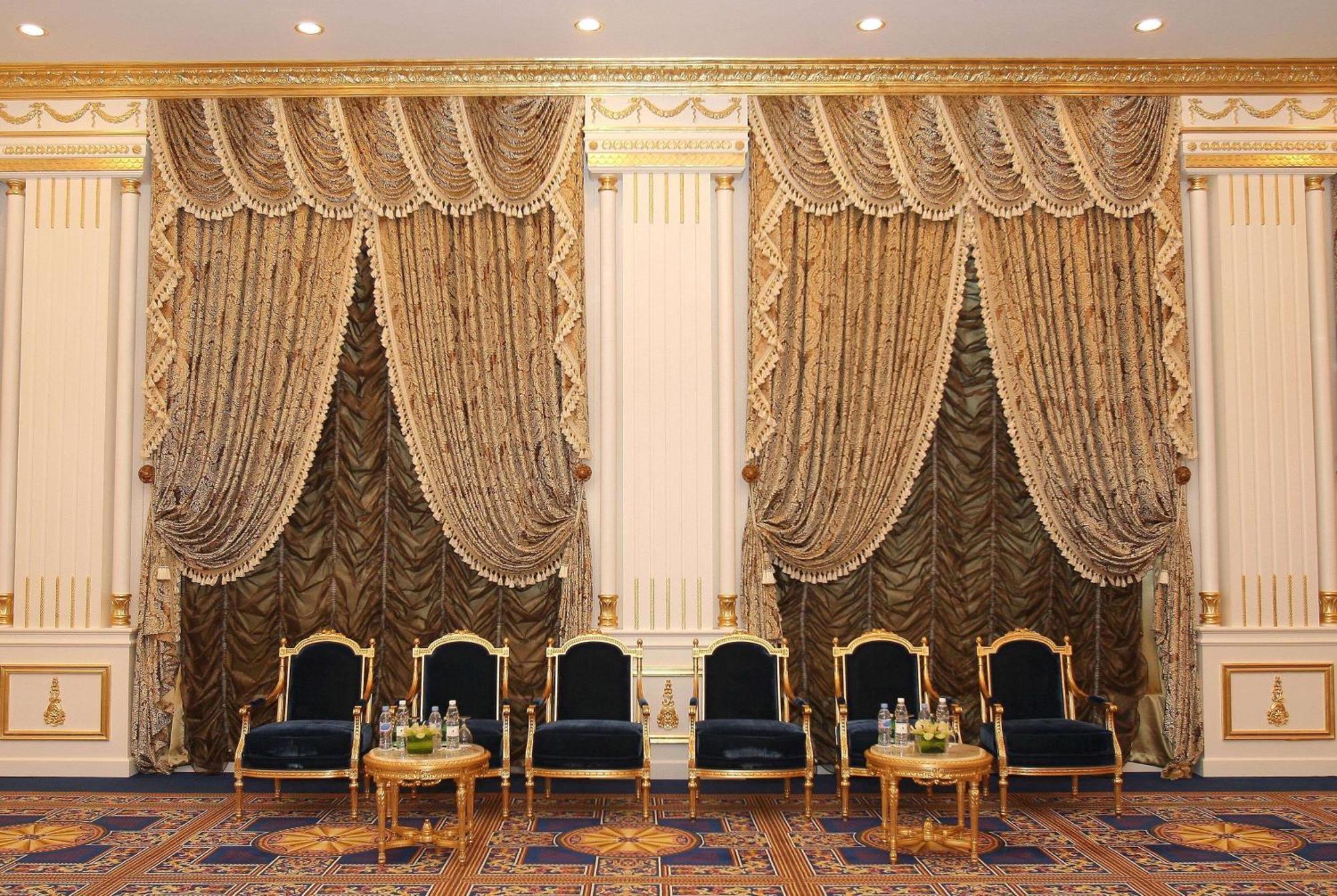 Grand Regency Doha, Trademark Collection By Wyndham Bagian luar foto The photo shows an elegantly decorated interior space. There are two sets of opulent curtains on the walls, featuring rich fabrics with ornate designs and gold accents. The curtains are paired with decorative tiebacks. In front of the curtains, there