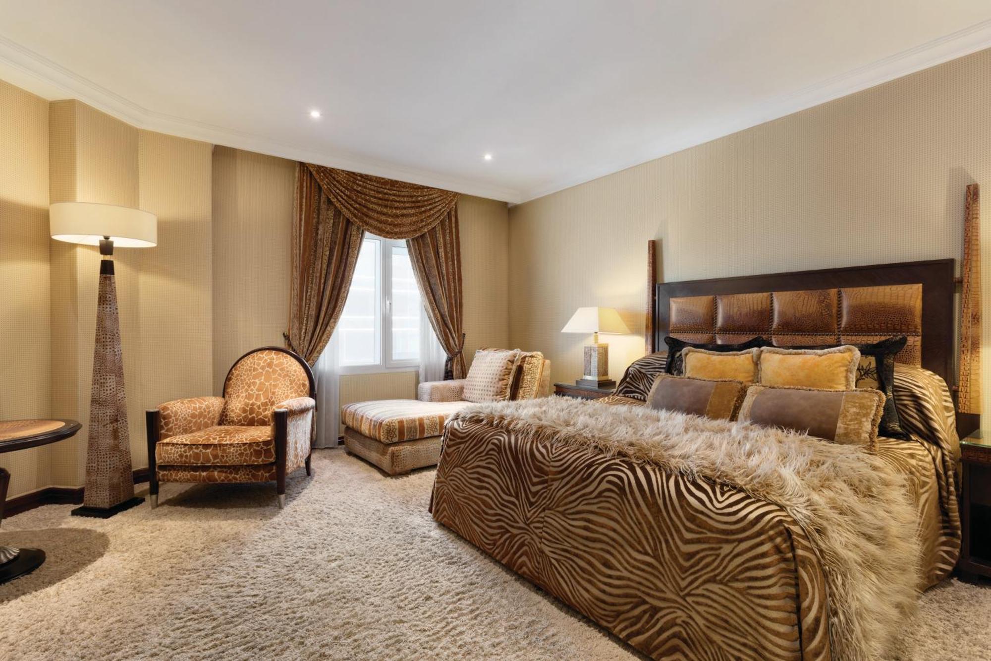 Grand Regency Doha, Trademark Collection By Wyndham Bagian luar foto The photo shows a stylishly decorated bedroom. The focal point is a large bed dressed in fabrics with a rich, textured appearance, possibly featuring a zebra print or similar design. On either side of the bed, there are small bedside lamps. 

Adjacen