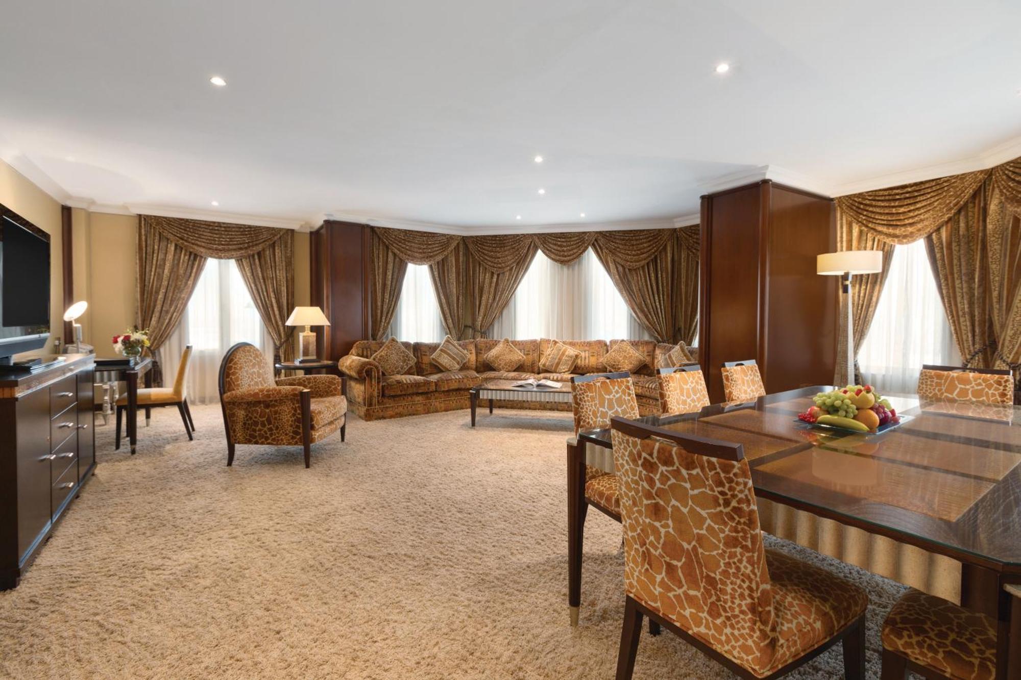 Grand Regency Doha, Trademark Collection By Wyndham Bagian luar foto The photo shows a spacious and elegantly designed living area. There are large windows dressed with luxurious curtains, allowing natural light to fill the room. The seating arrangement features a comfortable sofa with various cushions and several sty