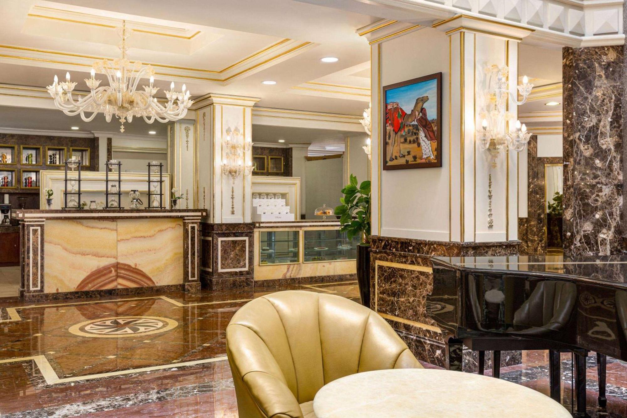 Grand Regency Doha, Trademark Collection By Wyndham Bagian luar foto The photo depicts an elegant hotel lobby interior. It features a polished marble floor with intricate patterns. In the background, there is a reception desk made of marble and wood, with decorative elements and a glass display. On the walls, you can 