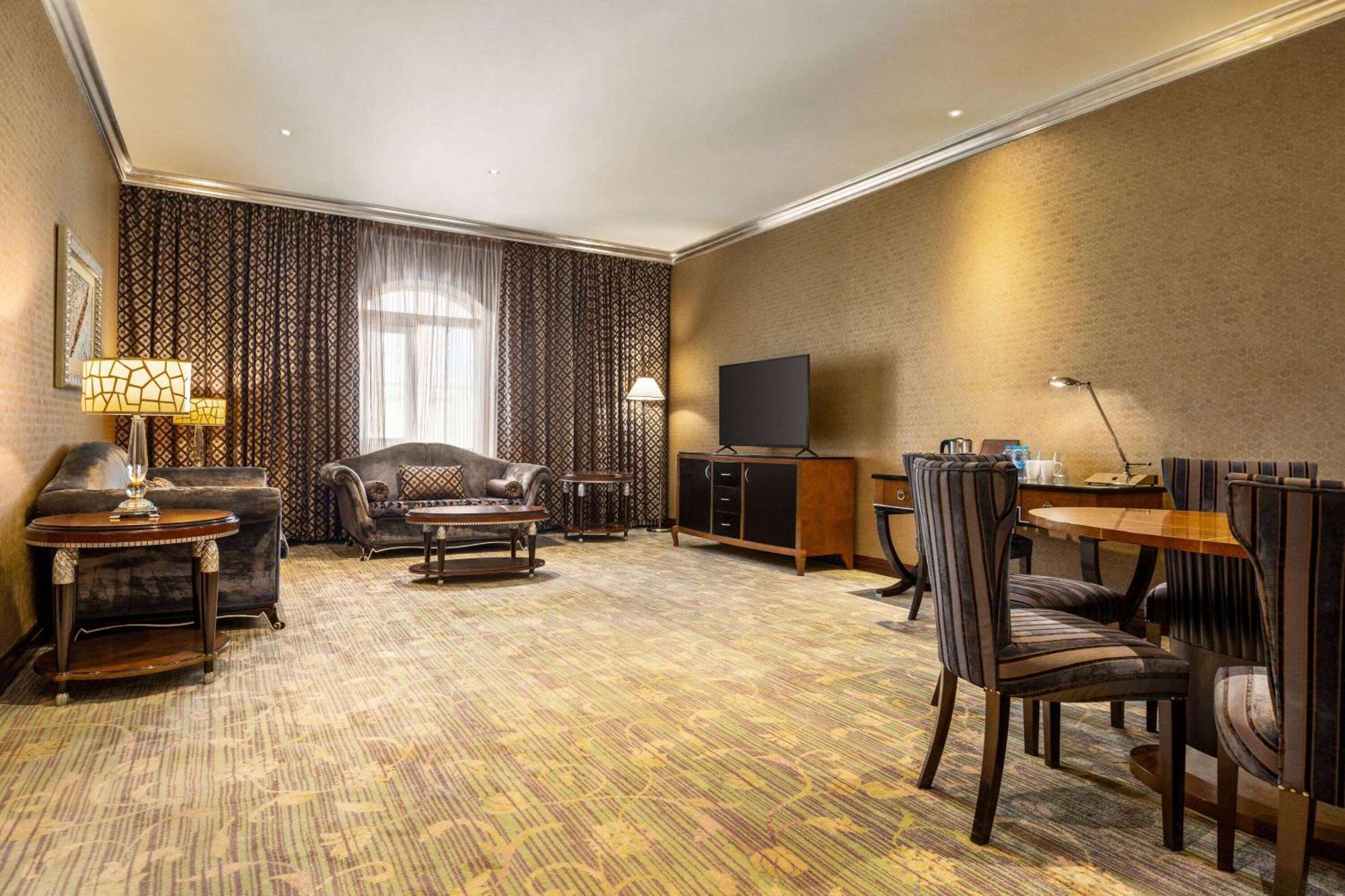 Grand Regency Doha, Trademark Collection By Wyndham Bagian luar foto The photo shows a spacious lounge or living area. It features a comfortable seating arrangement with a dark-colored sofa and armchairs, arranged around a coffee table. There's a dining table with matching chairs, suggesting it can accommodate meals o